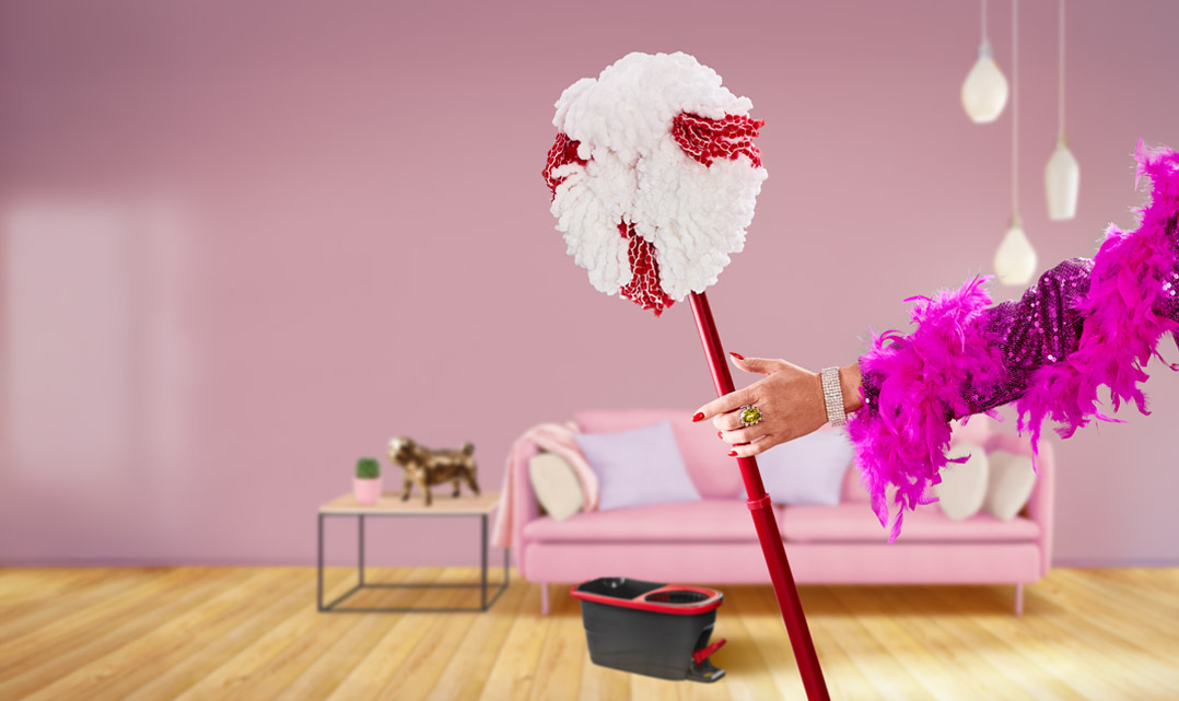 Arm i paljettkavaj och fjäderboa håller en Vileda-mopp i ett färgglatt vardagsrum.