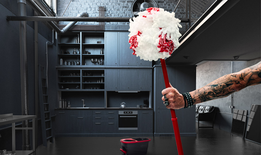 Tatuerad arm med nitarmband håller en Vileda-mopp i ett svart kök.
