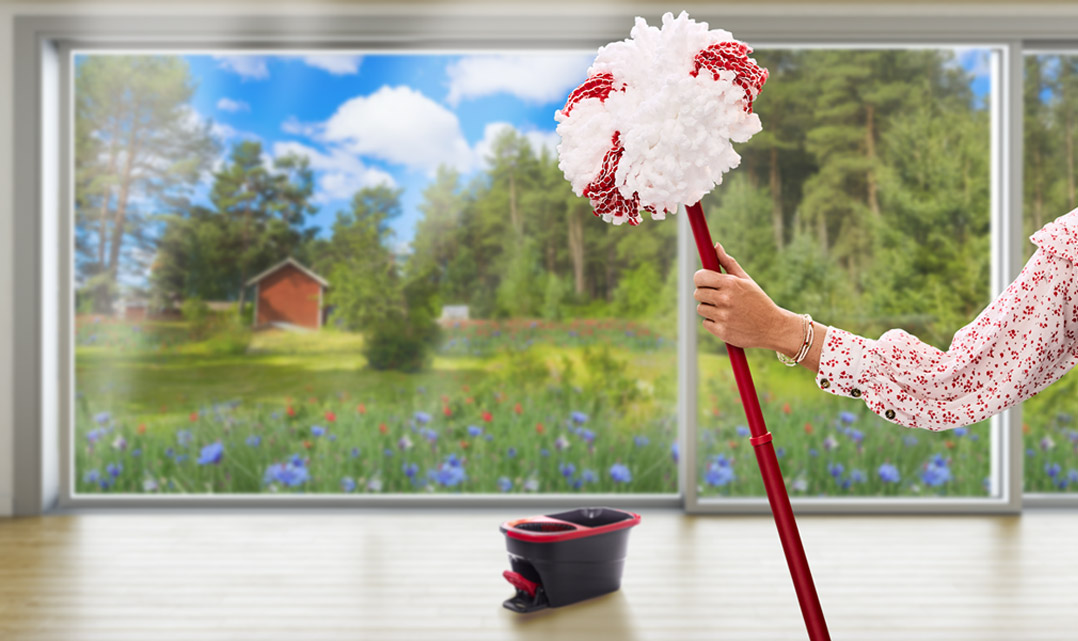 Arm i sommarblus håller en Vileda-mopp med sommaräng i bakgrunden.